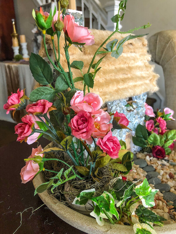 Indoor fairy garden with faux roses and a handcrafted fairy cottage.