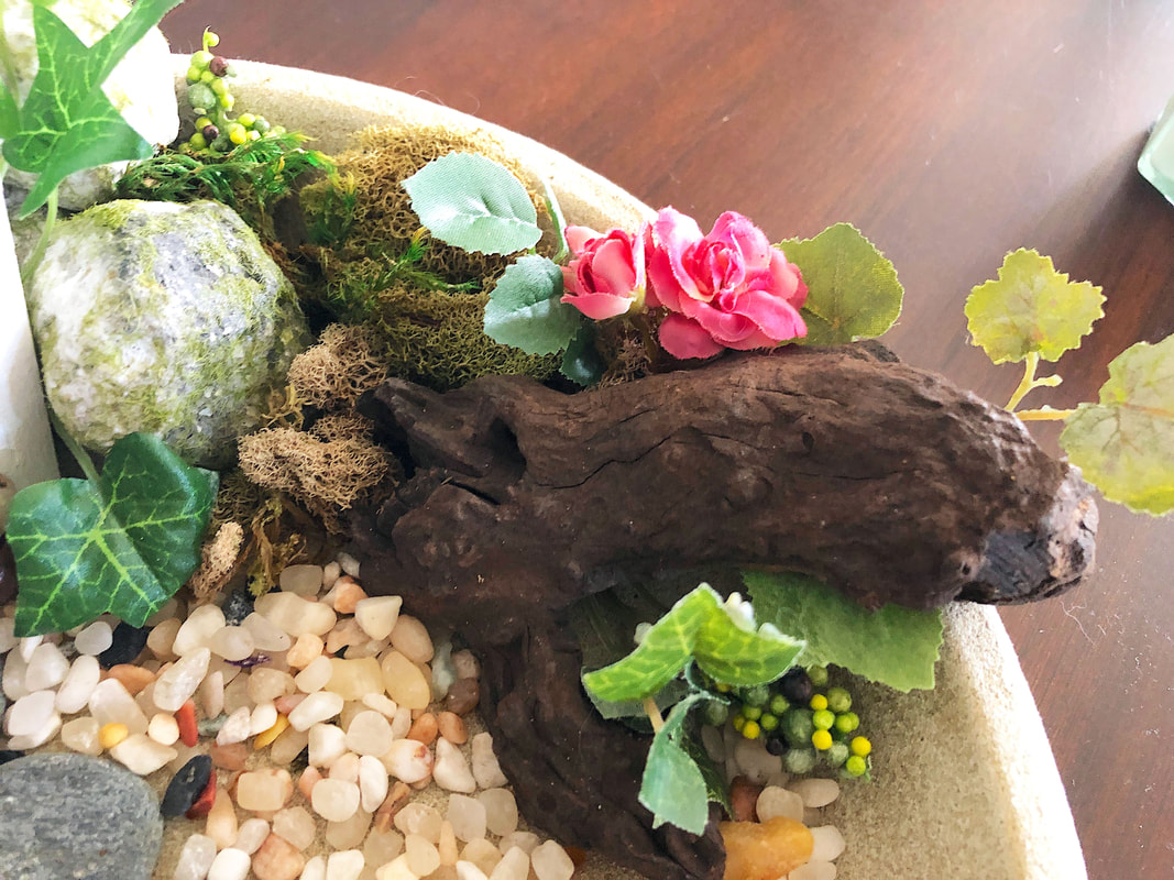 Closeup of indoor fairy garden florals and pebbles.